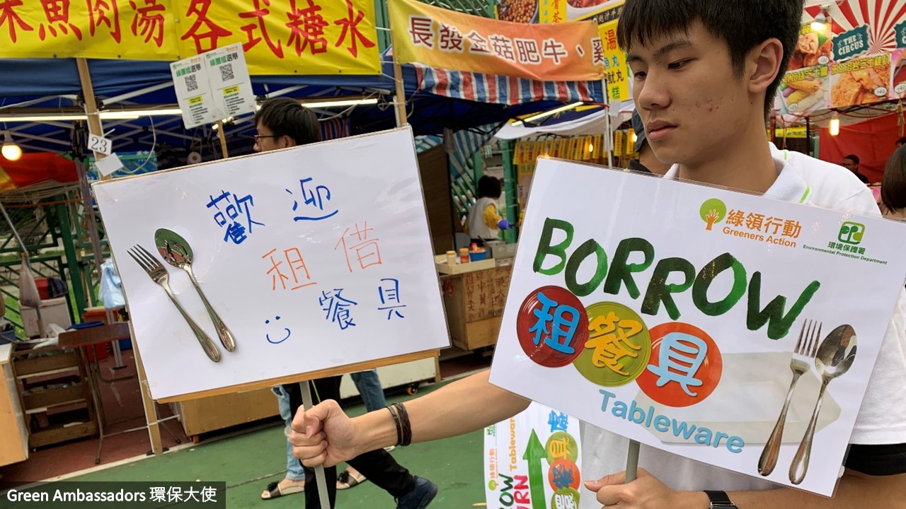 A green ambassador is holding a signage of "Borrow reusable tableware"